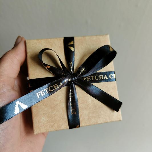 Image shows the Fetcha Chocolates handmade box of four dark filled chocolates closed box. The kraft box is finished with black and gold ribbon. This is the plastic free packaging for vegan, dairy free, gluten free and soy free chocolates.