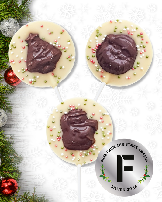 Three vegan chocolate lollipops with decorative sprinkles on a white surface with Christmas decorations.