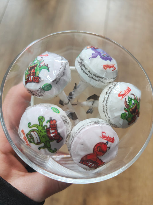 Image shows 5 lollipops with monsters on thier wrapping contained in a clear container, being sold by Fetcha Chocolates