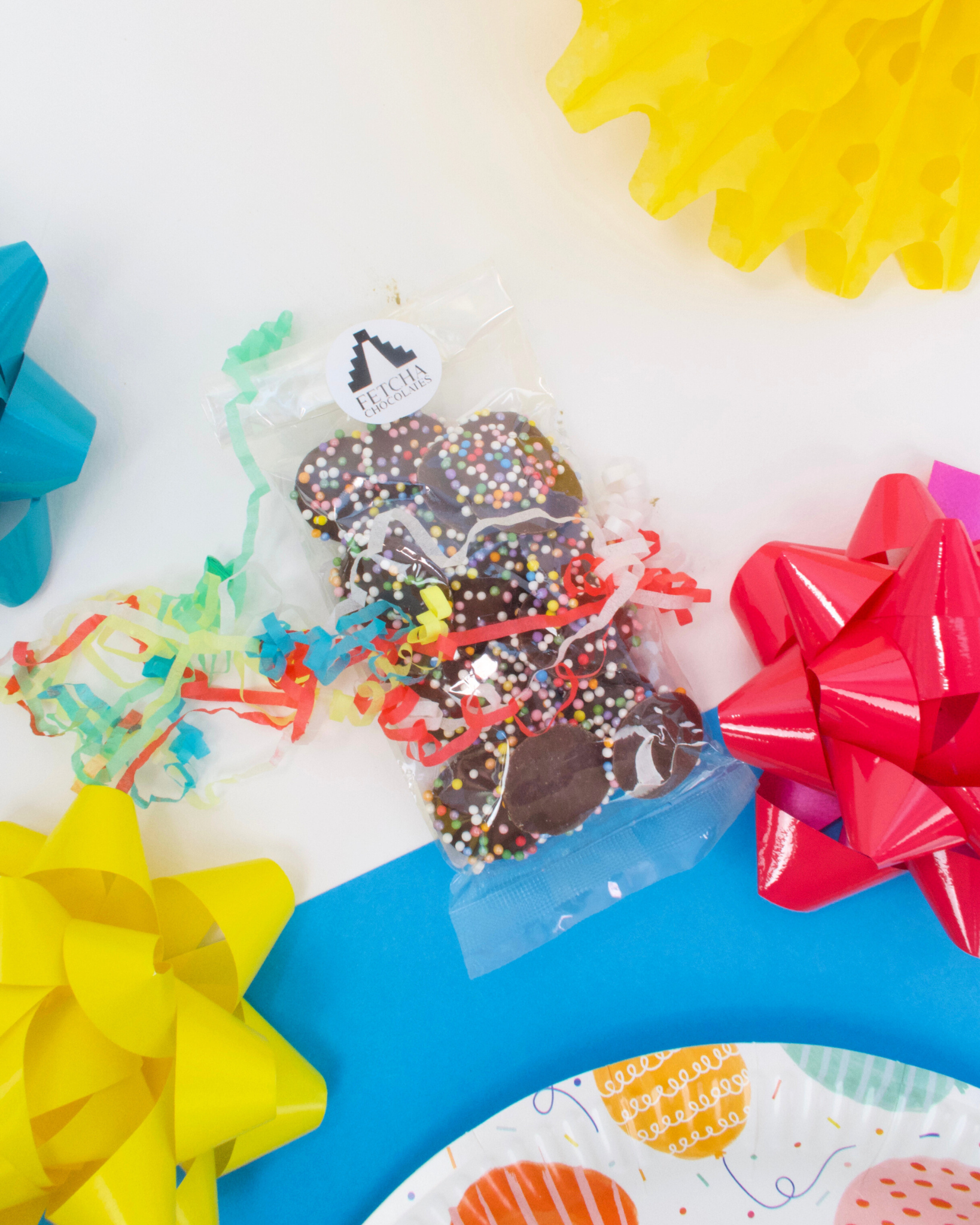 A clear package of multicoloured vegan chocolate drops with sprinkles on a table with colourful party decorations