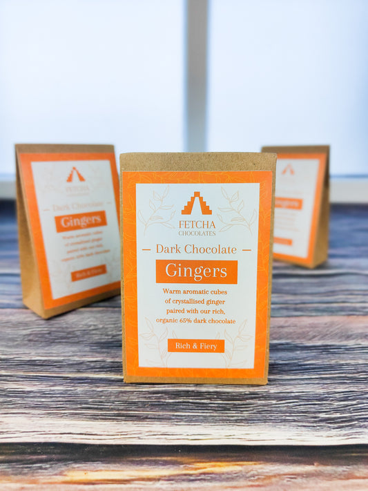 Image shows Fetcha Chocolates handmade dark chocolate gingers,  which are vegan, dairy free, gluten free and come in plastic-free packaging. The packaging is brown kraft cardboard with an orange label. 