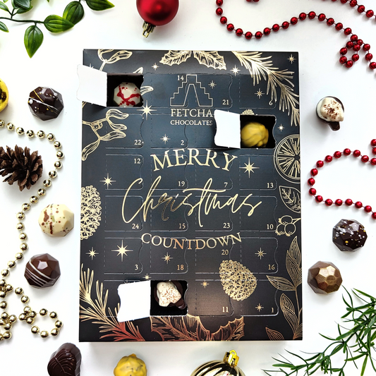 Black and Gold Advent Calendar with luxury vegan chocolates and Christmas decorations dotted around it